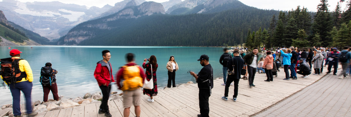 Multiple groups of visitors crowd the Lake Louise lakeshore taking photos and selfies