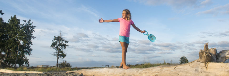 On the sandy expanse of Sidney Spit, a driftwood tree becomes a natural balance beam for this girl. Gulf Islands National Park Reserve.