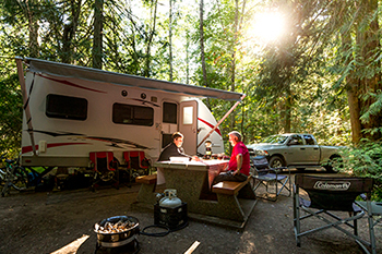 A man and a woman sitting at a picnic table in a campsite 