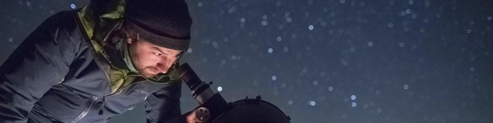 Un homme regarde dans un téléscope pendant la nuit.