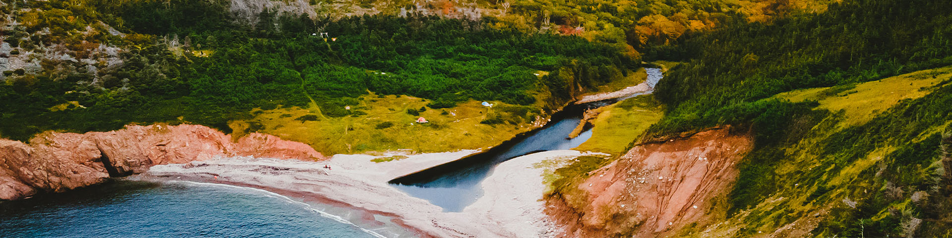 An aerial photo of a cove with tents nestled in the grass and trees by a river next to the ocean