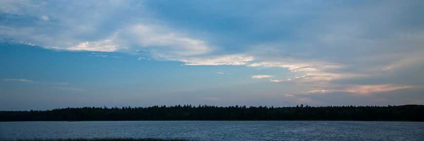 Blue skies over a calm Kejimkujik lake, with a dark tree line in the distant background.