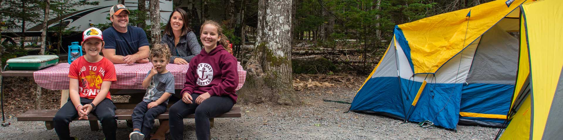 A family sitting at a picnic table next to a tent.