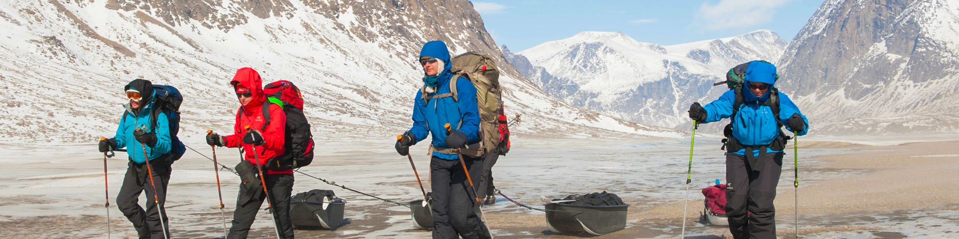 Four people hiking with pulk sleds in the Akshayuk Pass