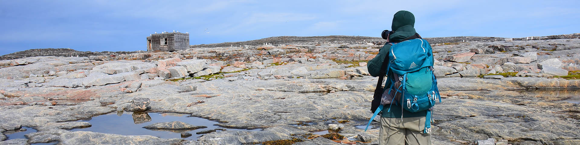 A person wearing a backpack taking a photo of an old building on a rocky landscape. 