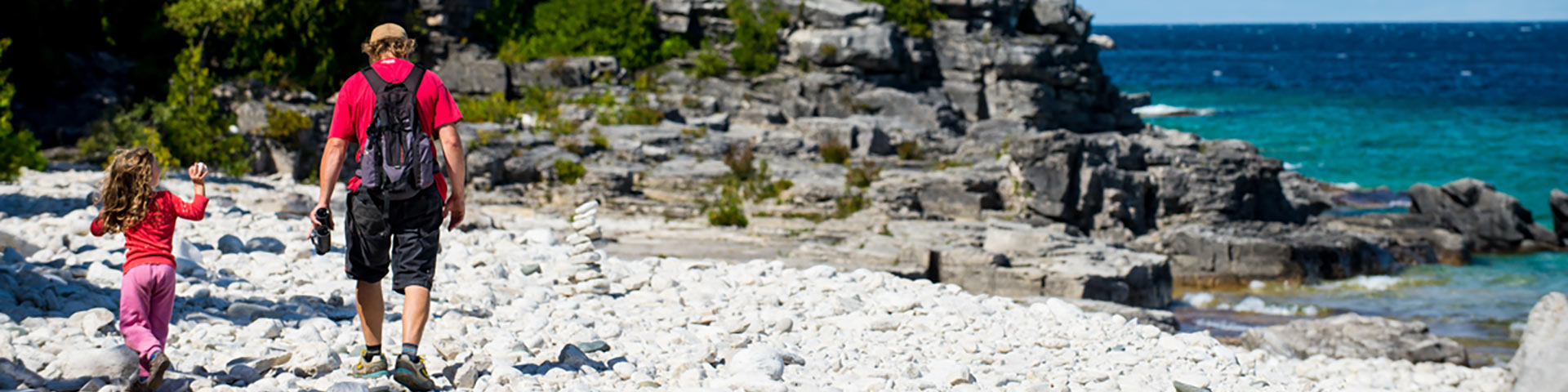 Two visitors hike along a rocky shoreline. 