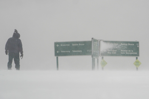 A person standing in a snow storm near a sign