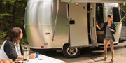 A man and a woman outside of a camping trailer.