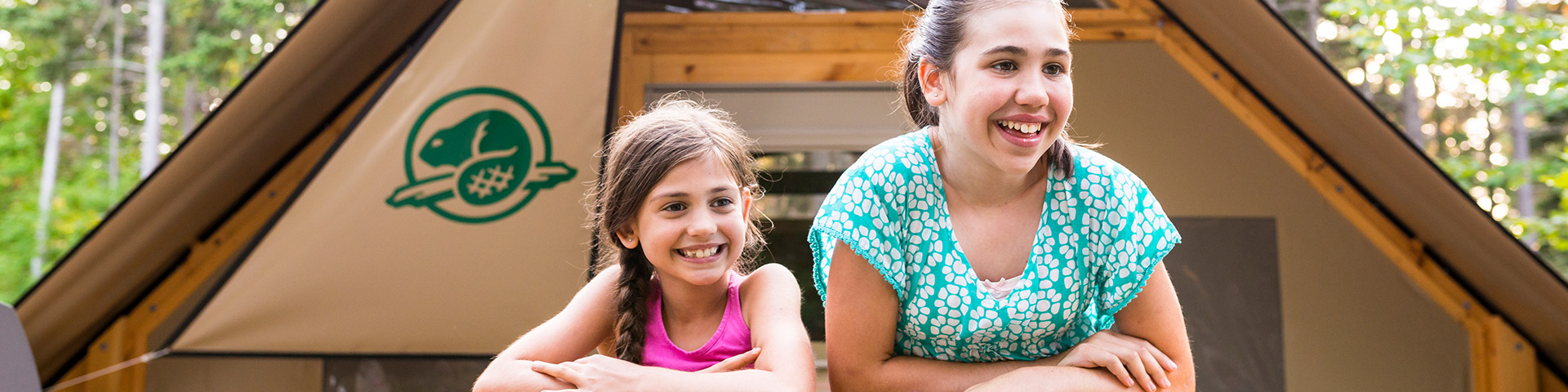 Two young sisters relax on the deck of an oTENTik at Stanhope Campground. Prince Edward Island National Park.