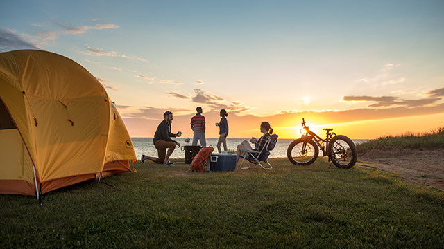 A group of friends enjoy the sunrise outside their tent at Cavendish Campground. Prince Edward Island National Park.