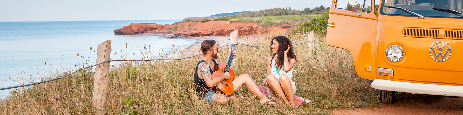 Couple play a guitar beside a retro minibus along the coast near Cavendish on a summer day. Prince Edward Island National Park