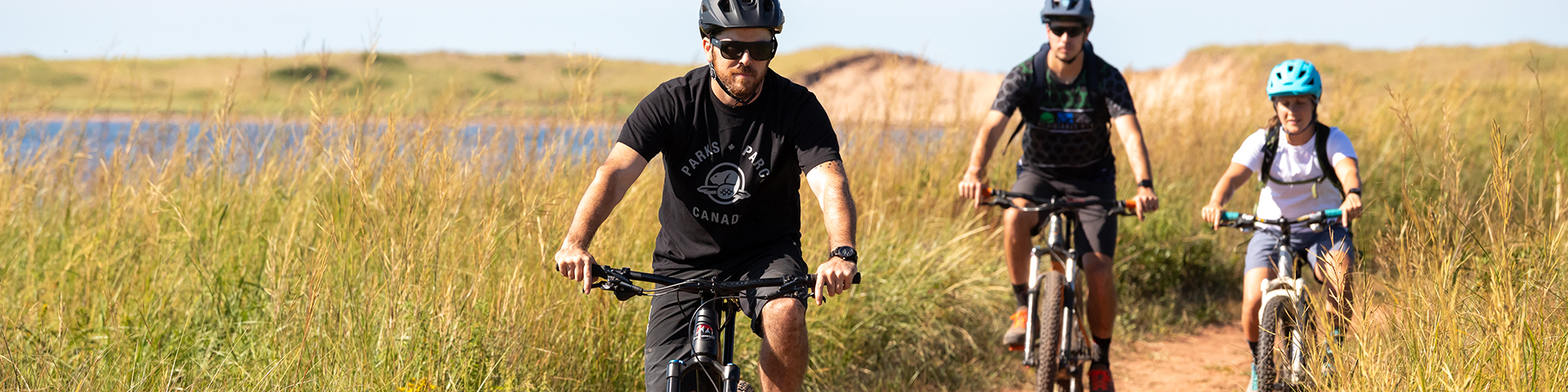 Three people cycling along a dirt path by the dunes in PEI National Park