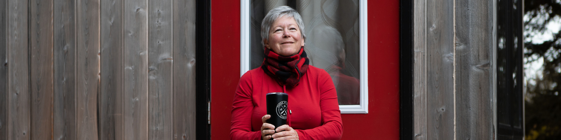 A smiling woman holding a mug is sitting at the doorstep of the microcube.  