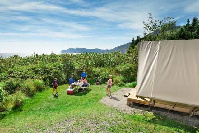 A family is gathered around a prospector-type tent, enjoying themselves. 