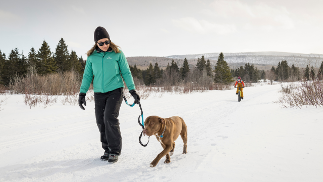 A woman walks with her dog on a winter trail. 