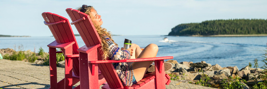 Young woman lounging in front of Île du Havre, sitting on a red chair in Havre-Saint-Pierre.