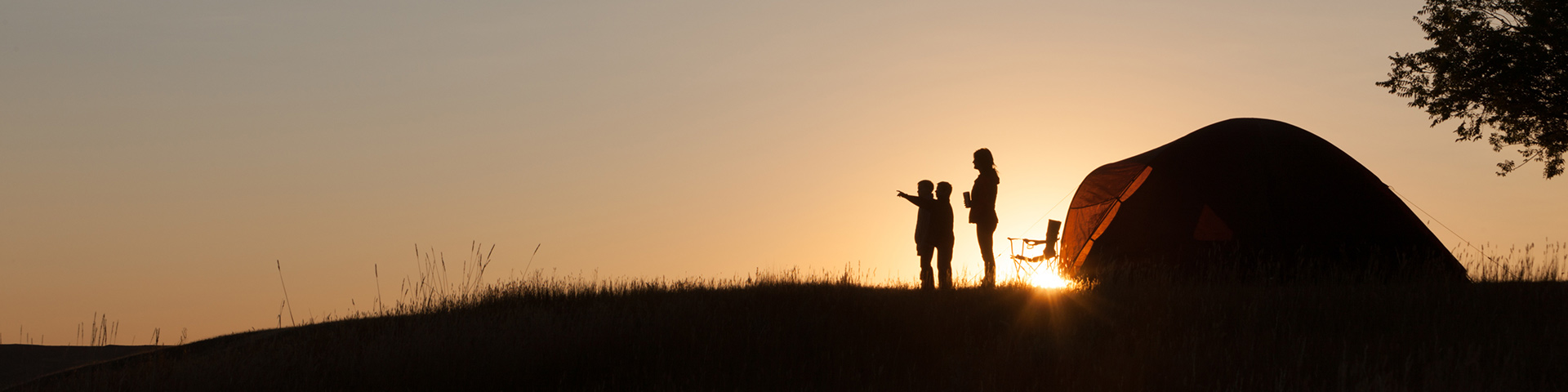 A small family camping, observing the sunset. 