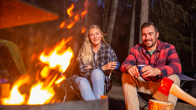 A young adult group of friends hang out around a campfire at their campsite at Beaver Glen Campground during the summer in Prince Albert National Park.