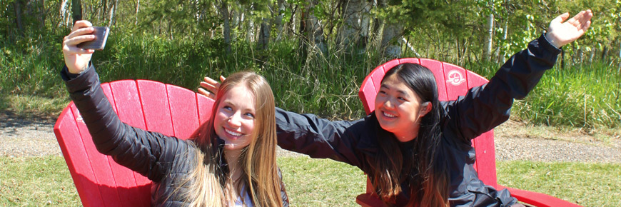 Two young ladies take a “selfie” while sitting in Parks Canada red chairs. 