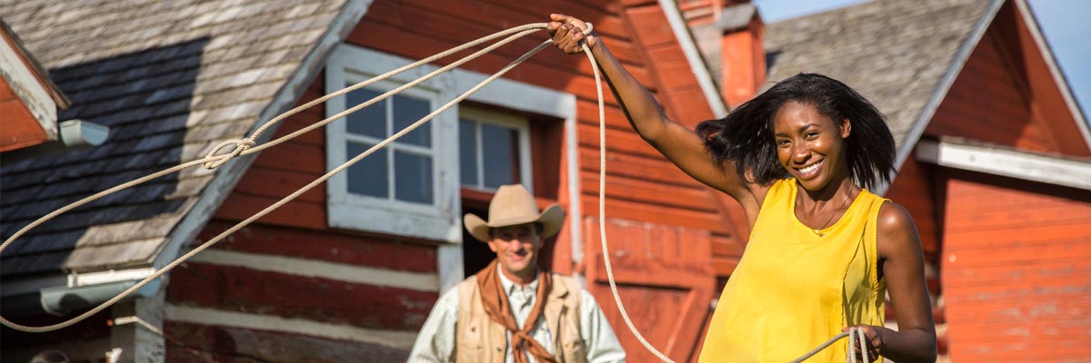 Un guide est à côté d’une jeune femme qui tire au lasso au lieu historique national du Ranch-Bar U.