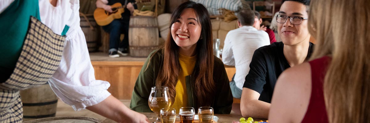 Trois adultes se font servir à boire par une guide en costume d’époque à la taverne de la forteresse de Louisbourg.