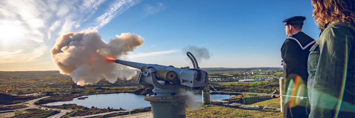 Deux adultes debout derrière un canon qui fait feu sur la colline au lieu historique national de Signal Hill.