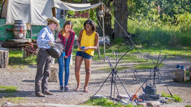 A Parks Canada interpreter pours cowboy coffee for two young women at roundup camp, Bar U Ranch National Historic Site.