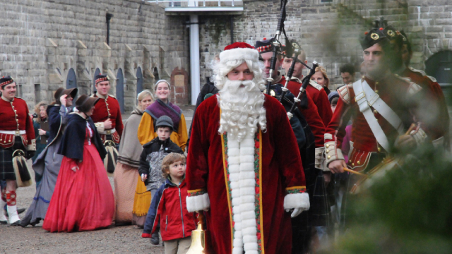 Des guides en costume d'époque derrière un homme déguisé en père Noël dans un fort historique.