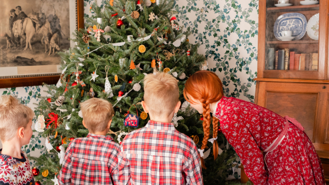 Une guide costumée, personnifiant Anne de la maison aux pignons verts, regarde un sapin de Noël avec trois garçons avec des vêtements festifs.