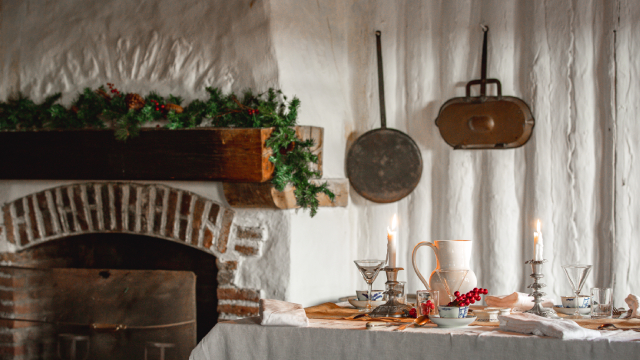 Une table où il y a des bougies, des assiettes, des ustensiles et divers objets devant une cheminée décorée de façon festive et ornée d'une guirlande. 