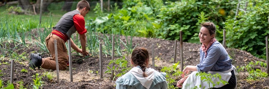 Trois guides en costume d’époque travaillent dans le jardin de la maison Riel.