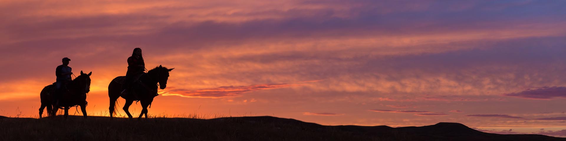 Two visitors on horseback during sunset.